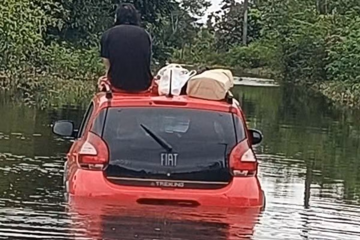 Motorista sobe em teto de carro após ficar ilhado durante enchente no litoral de SP